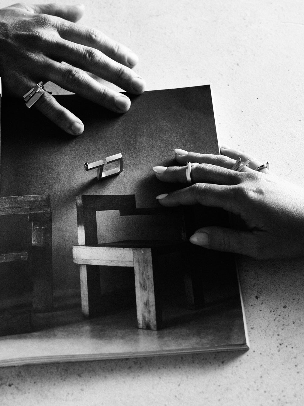 Black and white photo of hands holding a book with geometric wood models.